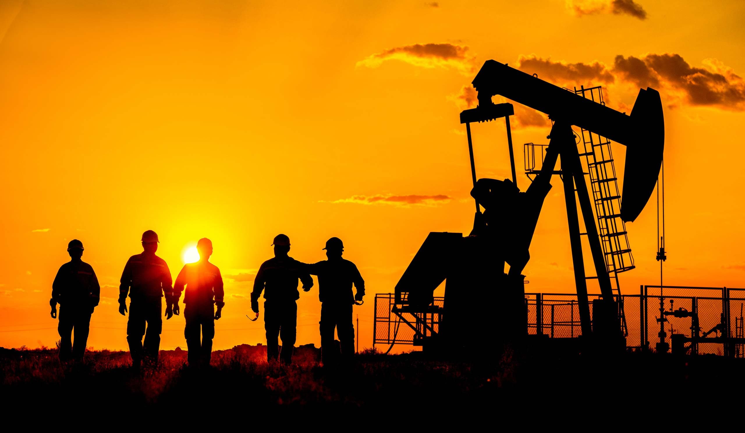 Oilfield workers walking toward pumpjack at sunset